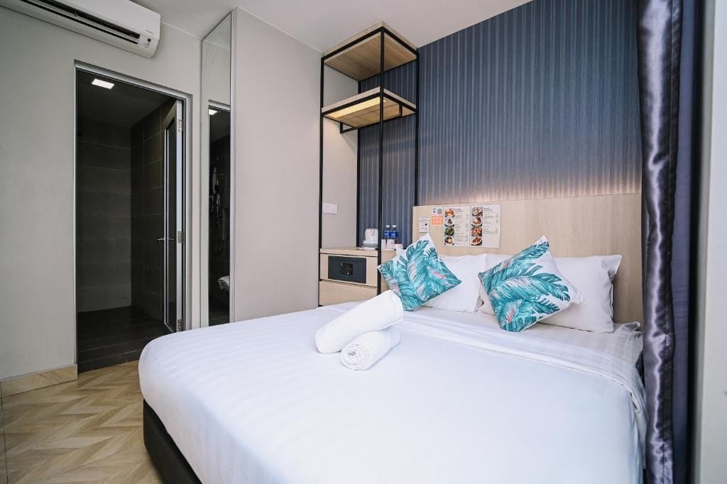 A hotel room with a bed, a nightstand, a mirror, a wall with a vertical panel, and a door leading to a bathroom.