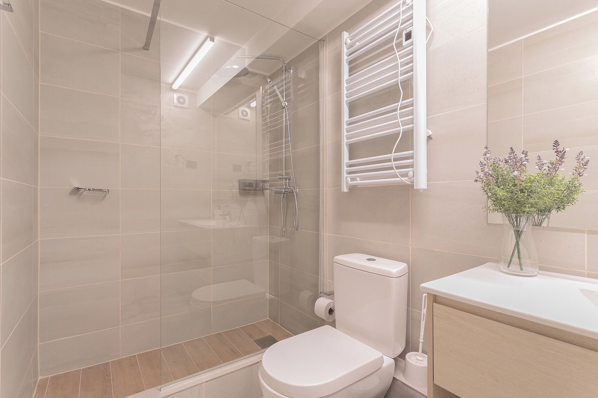 A modern bathroom with a glass-enclosed shower, a toilet, and a sink with a vase of flowers.