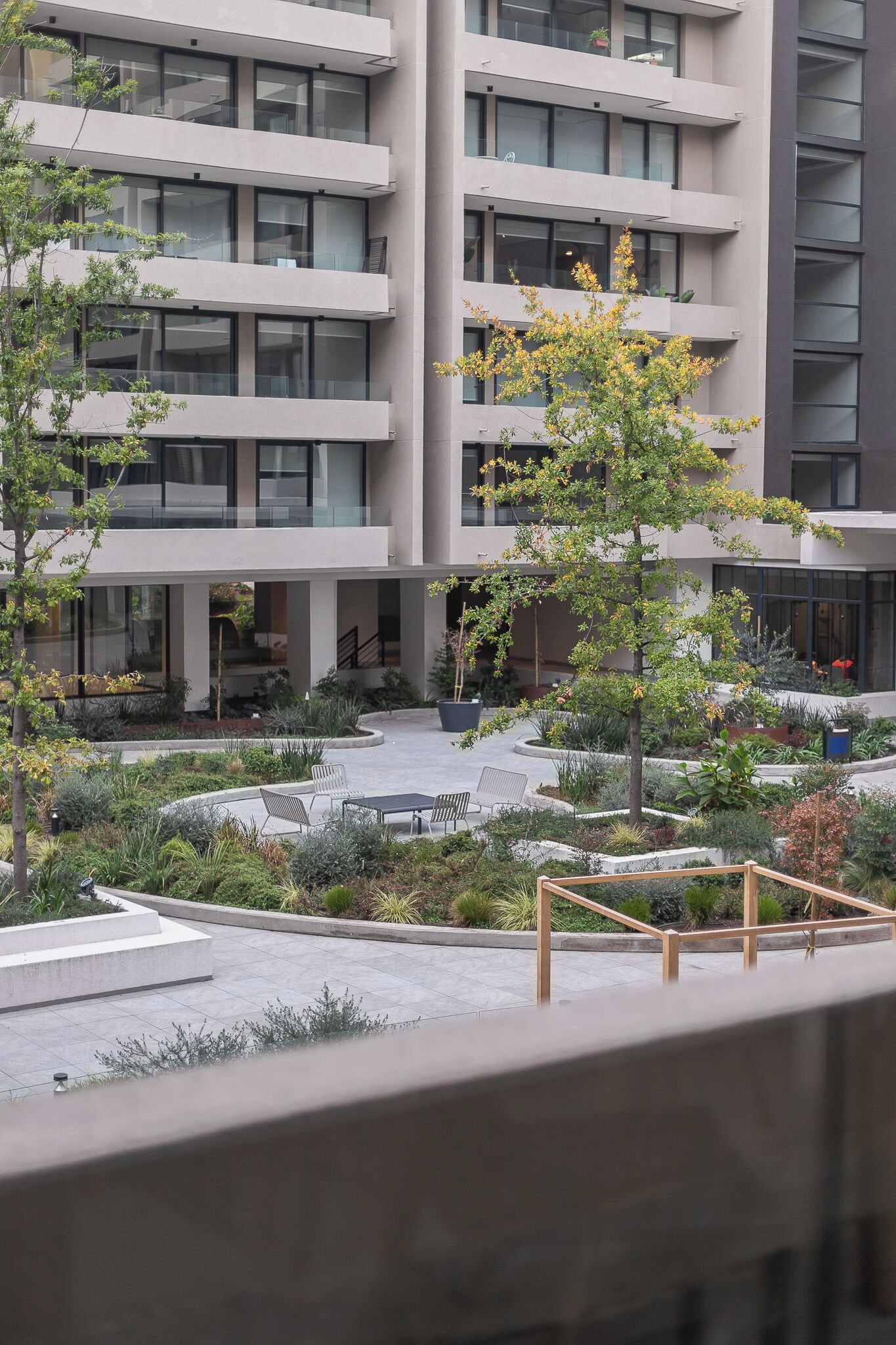 A modern building with multiple floors, a courtyard with seating, and a variety of plants.