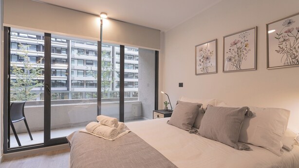 Un dormitorio moderno con una cama grande, una silla y un balcón con vistas a un edificio.