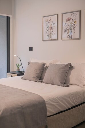 Ein Schlafzimmer mit einem Bett, zwei Kissen, einem Nachttisch mit Lampe und zwei gerahmten floralen Kunstwerken an der Wand.