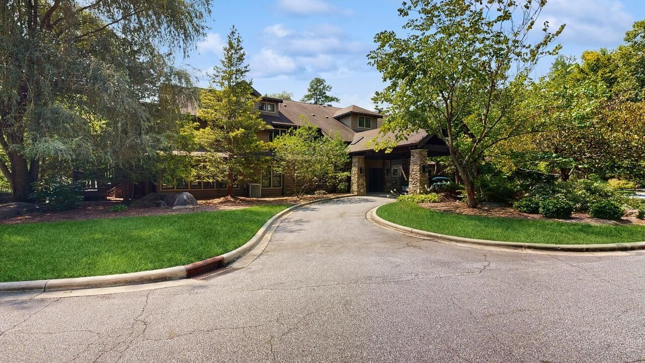 A residential driveway leading to a house with a stone entrance, surrounded by well-maintained lawns and trees.
