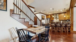 A dining area with a wooden table and chairs, a staircase, and wooden cabinets in the background. - Luxury Lakefront Condo, Gated Community, Mountain & Lake Views, Pool, Dock, & Kayaks (Lake Lure)
