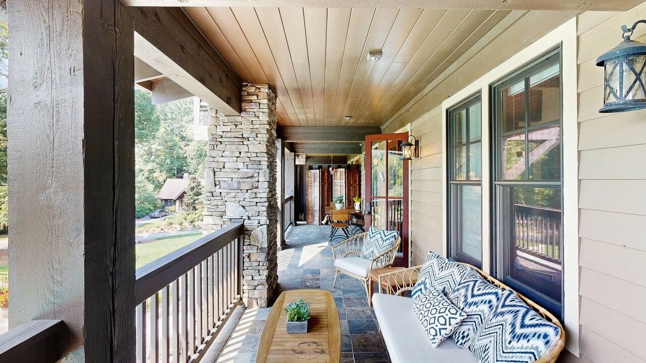 A covered porch with a stone wall, wooden ceiling, and a seating area with a sofa and chairs.