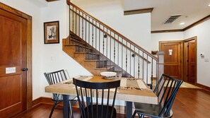 Un comedor con una mesa de madera, sillas negras y una escalera con barandas de madera.