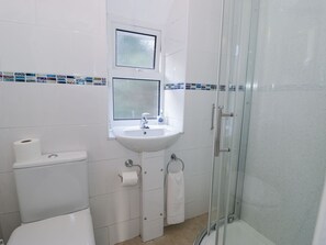 A bathroom with a toilet, sink, and glass-enclosed shower. - Ty Gwyn (Aberdovey)