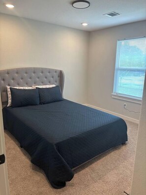 A bedroom with a tufted headboard, a dark blue bedspread, and a carpeted floor.