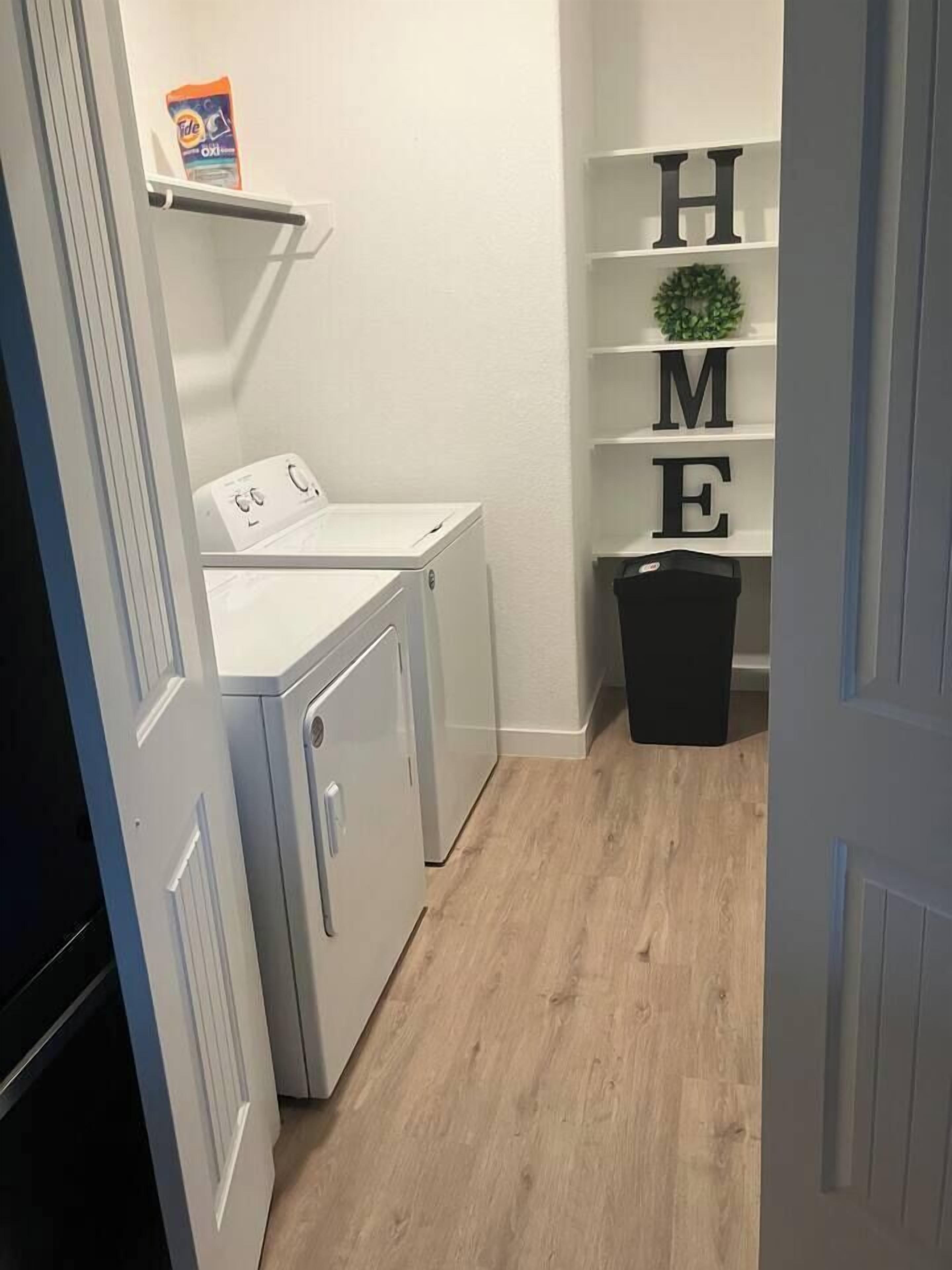 A laundry room with a washing machine, dryer, and a shelf with detergent.
