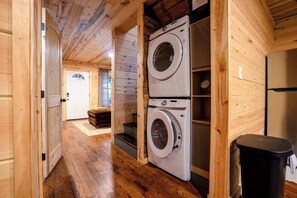 Une buanderie équipée de deux machines à laver superposées, avec un plancher en bois, une porte et une poubelle.