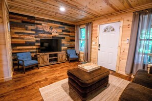 L’intérieur d’une cabine avec un mur en bois, un téléviseur, deux fauteuils, une table basse et une porte.