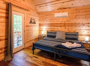 Ein Schlafzimmer einer Holzhütte mit einem Bett, einem Fenster, einer Tür und einer Klimaanlage.