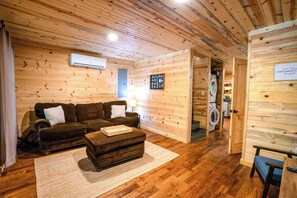 Interior acolhedor de uma cabana com piso de madeira, um sofá, uma mesinha e uma máquina de lavar ao fundo.