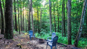 A forest with two Adirondack chairs and a fire pit. - Buttercup - Cozy Retreat - Central - WiFi (Gillmore)