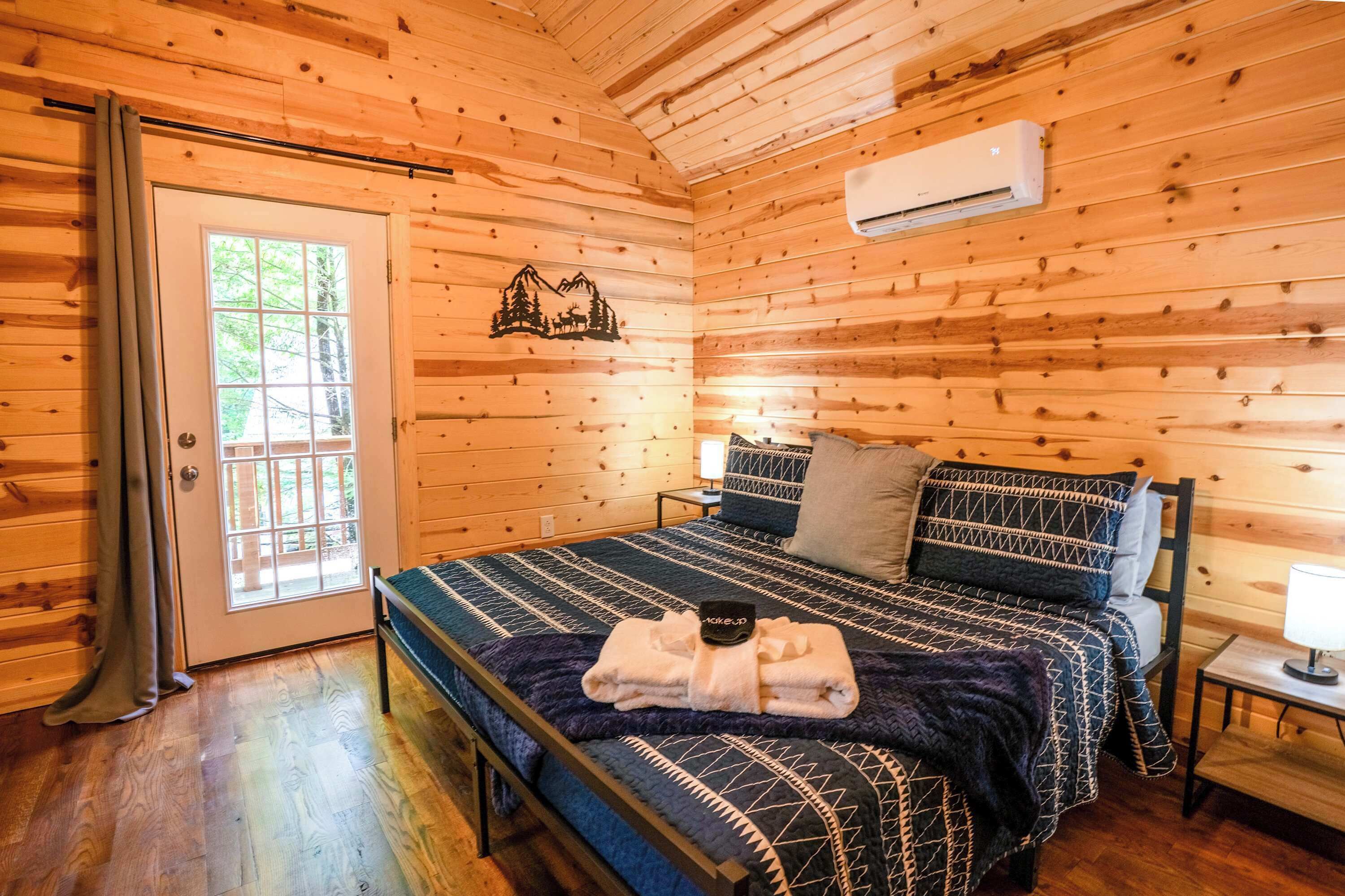 Une chambre dans une cabane en bois, avec un lit, une table de chevet, une lampe et une fenêtre.