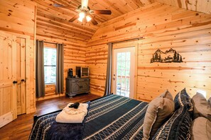 Interior de uma cabana de madeira com cama, cômoda e ventilador de teto.