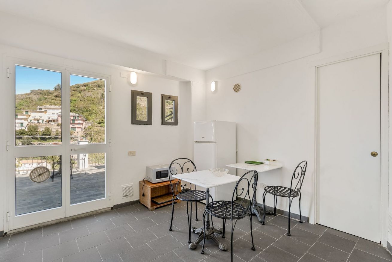 A room with a dining area, a white refrigerator, and a view through a glass door.