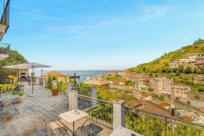 A terrace with outdoor seating, a view of the sea, and a hillside town in the background. - [StairwayToHeaven Room 1] 5Terre-Seaview (Riomaggiore)