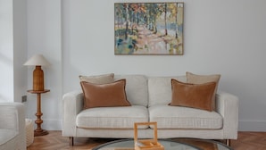Uma sala de estar com sofá, dois almofadas, abajur, pintura e mesa de centro.