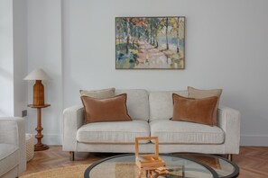 Ein Wohnzimmer mit einer Couch, zwei Kissen, einer Lampe, einem Gemälde und einem Couchtisch.