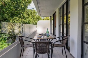Ein Balkon mit Korbstühlen und einem Tisch, mit Blick auf eine üppige Grünanlage.