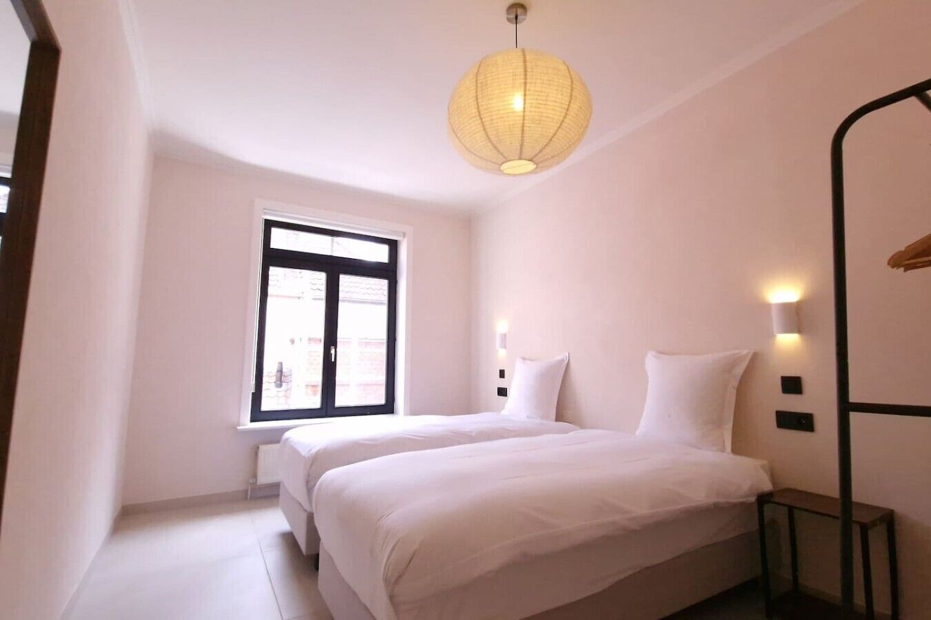 A bedroom with a large window, a bed, bedside tables, and a hanging light fixture.