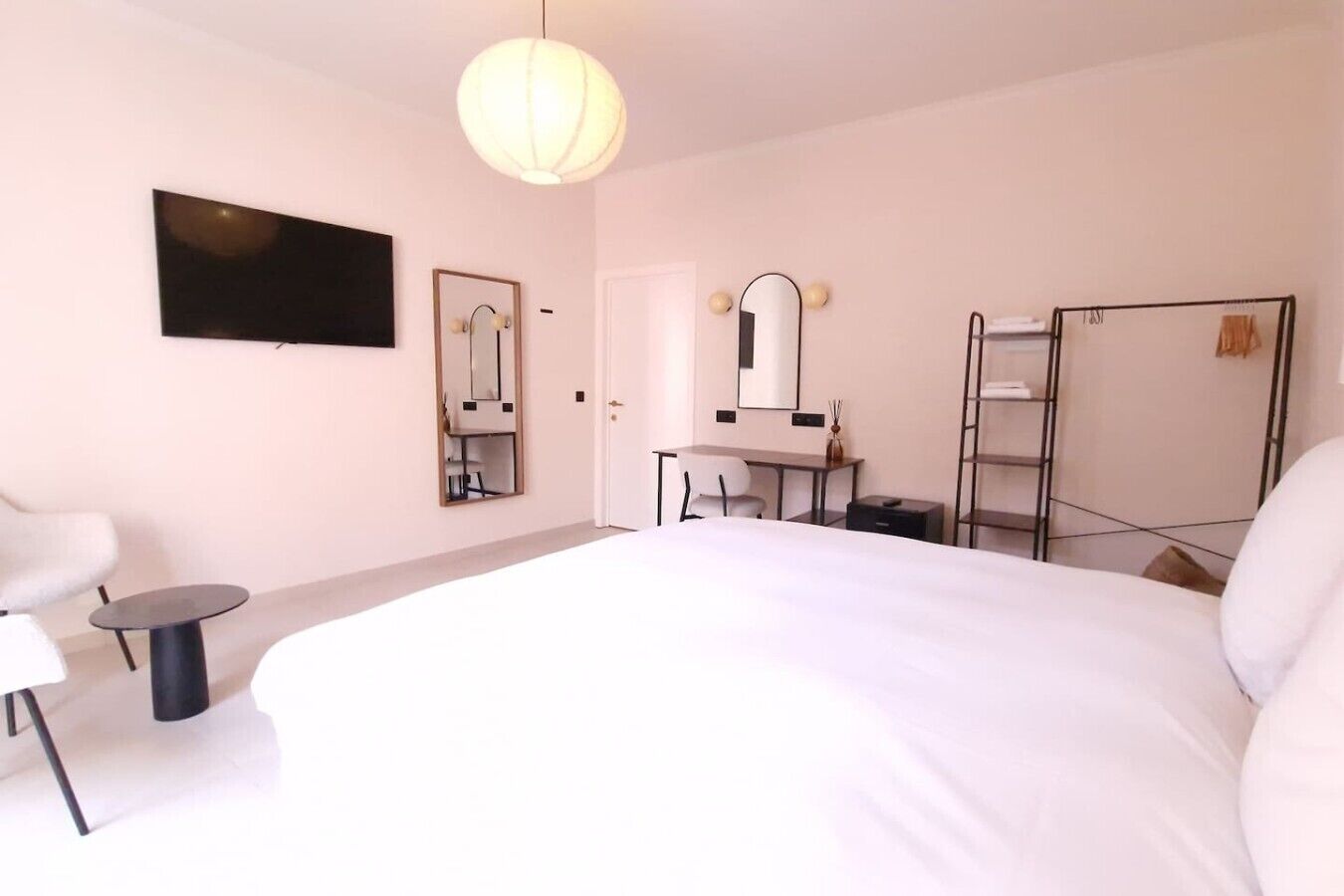 Une chambre d’hôtel avec un grand lit, un bureau avec une chaise, un miroir, un téléviseur fixé au mur et une armoire.