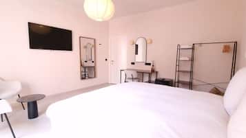 A hotel room with a large bed, a desk with a chair, a mirror, a TV mounted on the wall, and a wardrobe.