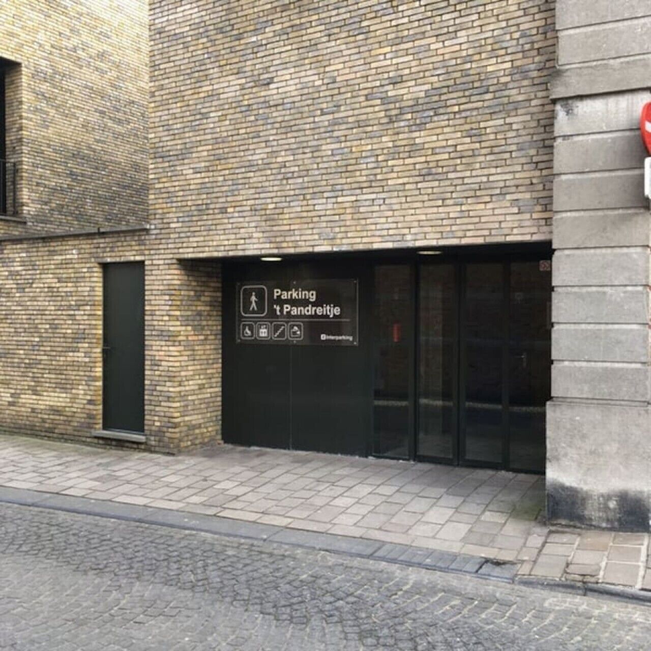Un bâtiment en briques avec une porte noire portant l’inscription « Parking et tarifs de stationnement » et un panneau indiquant les places de stationnement réservées aux personnes handicapées.