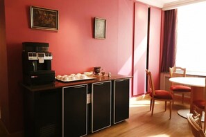 Una habitación con cafetera, una mesa con sillas y un ventanal con cortinas.