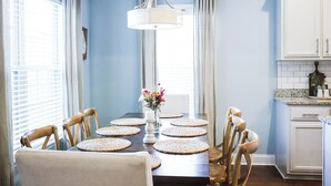 Comedor con una mesa dispuesta para seis personas, rodeada de sillas, un florero y una lámpara colgante.