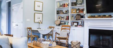 A living room with a fireplace, a television, and a bookshelf filled with books and decorative items.