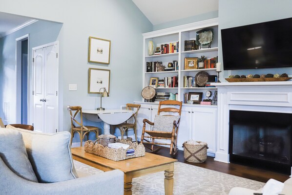 A living room with a fireplace, a television, and a bookshelf filled with books and decorative items.