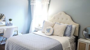Un dormitorio con cama, escritorio, silla, espejo y ventana con cortinas.