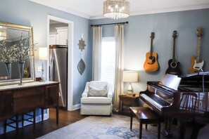 A room with a piano, a dining table with chairs, a mirror, and a refrigerator.