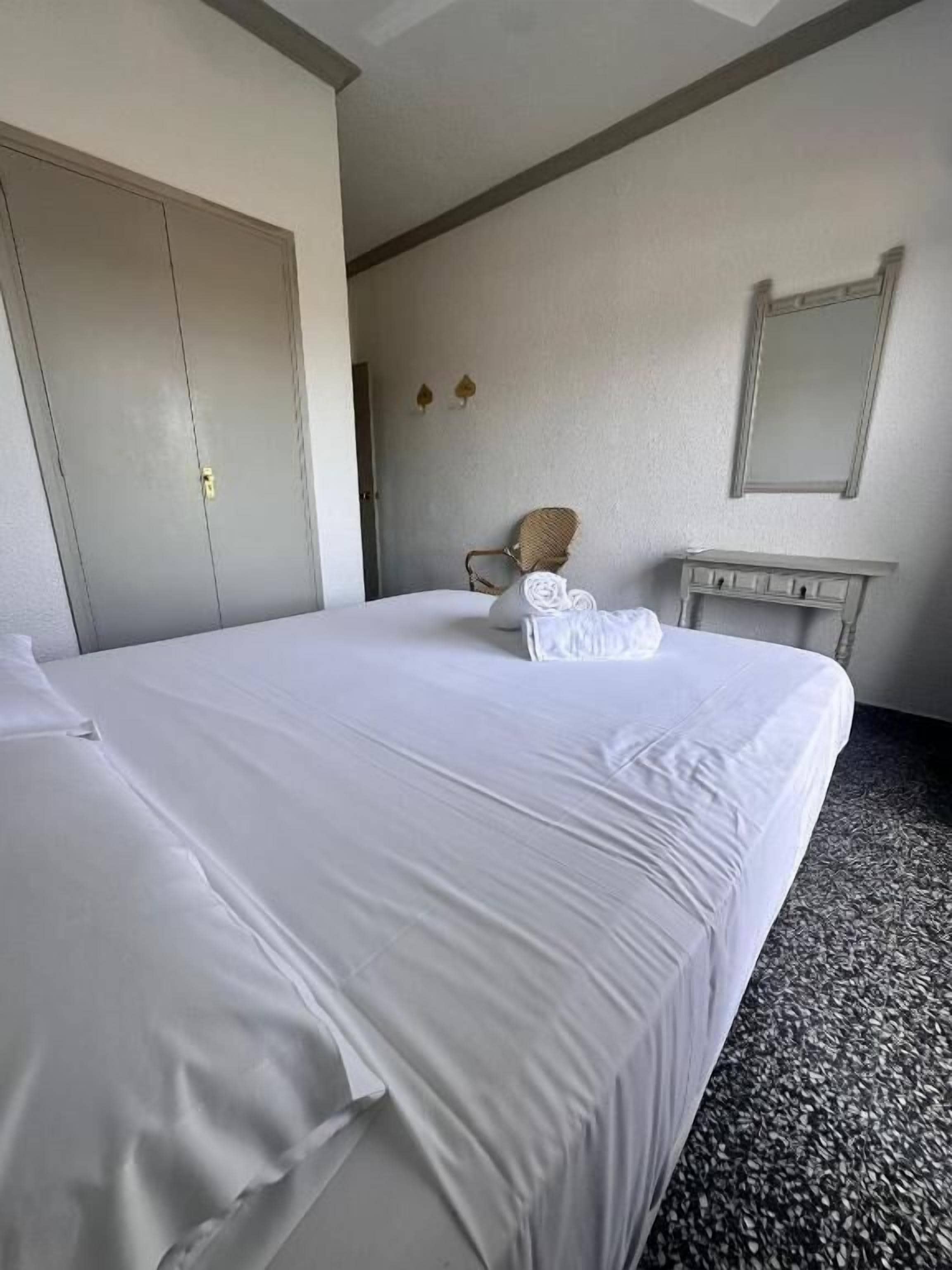 Quarto de hotel com uma cama grande, uma cadeira, uma mesinha e um guarda-roupa.