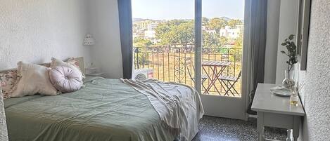 A hotel room with a bed, a desk, a chair, a balcony with a view, and an air conditioning unit.