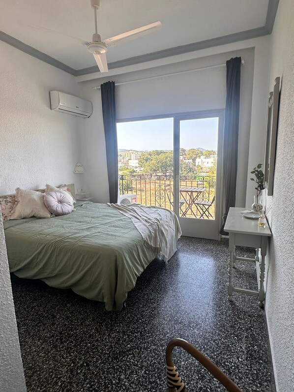 A hotel room with a bed, a desk, a chair, a balcony with a view, and an air conditioning unit.