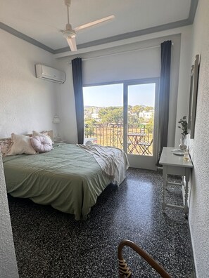 A hotel room with a bed, a desk, a chair, a balcony with a view, and an air conditioning unit.
