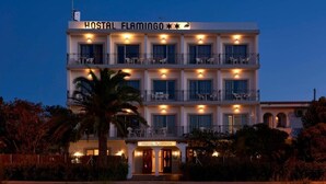 Un h ôtel à plusieurs étages, nommé « HOSTAL FLAMINGO », doté de balcons et d’un espace extérieur aménagé pour s’asseoir.