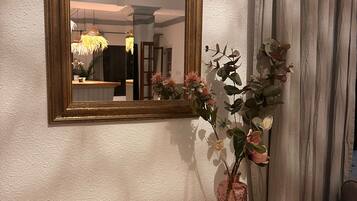 Une pièce avec un miroir, un vase rempli de fleurs, des bougies et un panier en osier posé sur une commode.