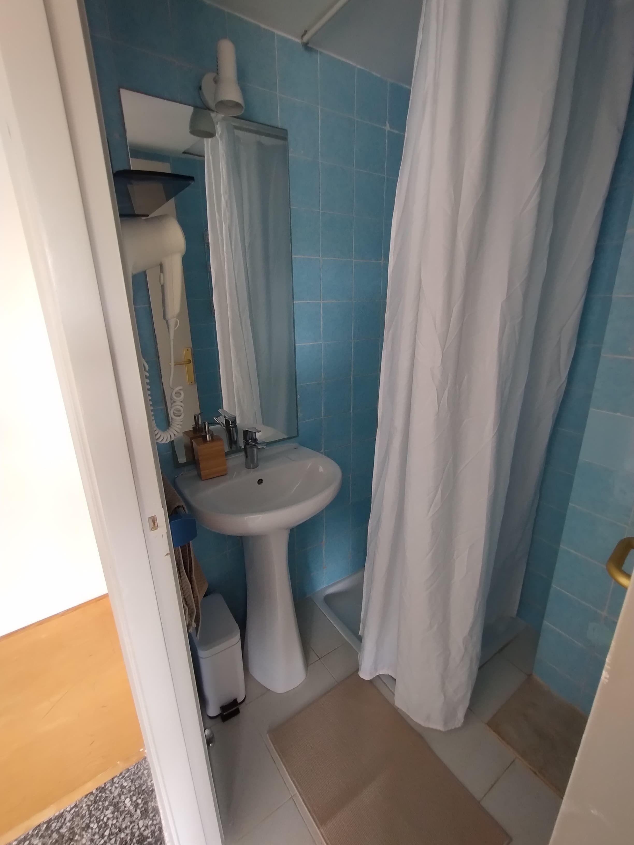 Een badkamer met een wit wastafeltje, een spiegel, een handdoekrek en een douchegordijn.