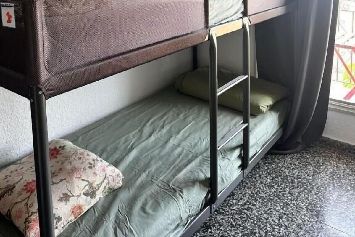 A bunk bed with a mattress and pillows, a window with a curtain, and an air conditioning unit on the wall.