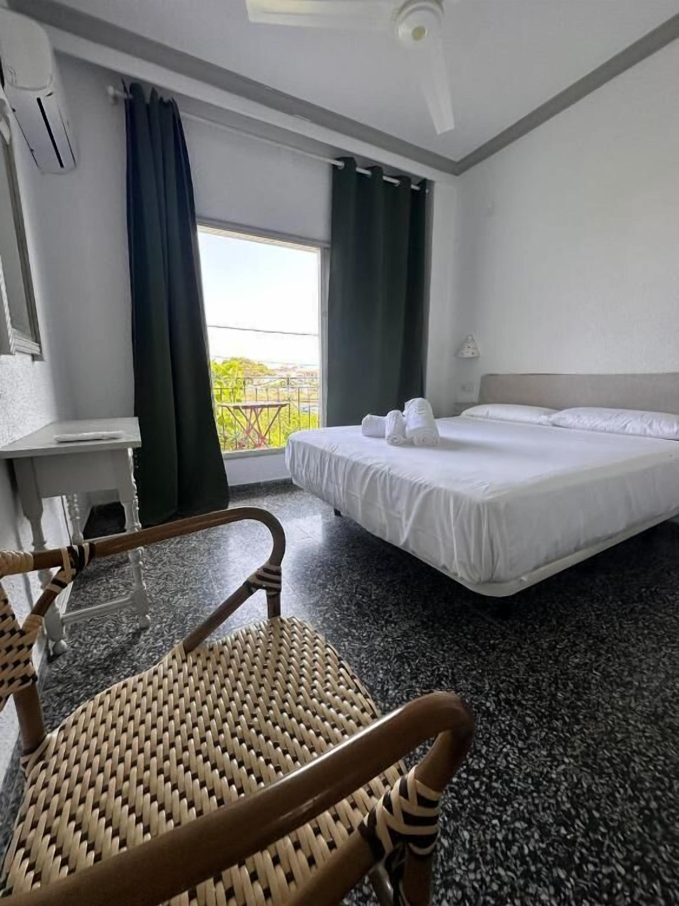 Una habitación de hotel con cama, una silla, un escritorio y una ventana con cortinas.