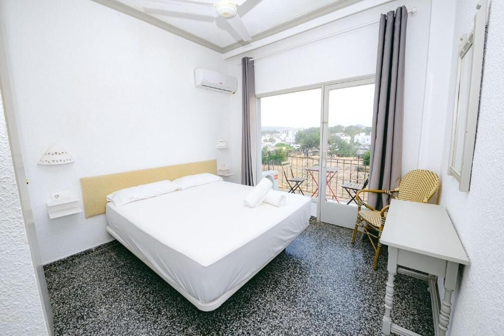 Quarto de hotel com cama, uma mesa pequena, uma cadeira e vista para o exterior.