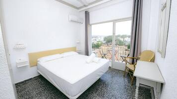Quarto de hotel com cama, uma mesa pequena, uma cadeira e vista para o exterior.