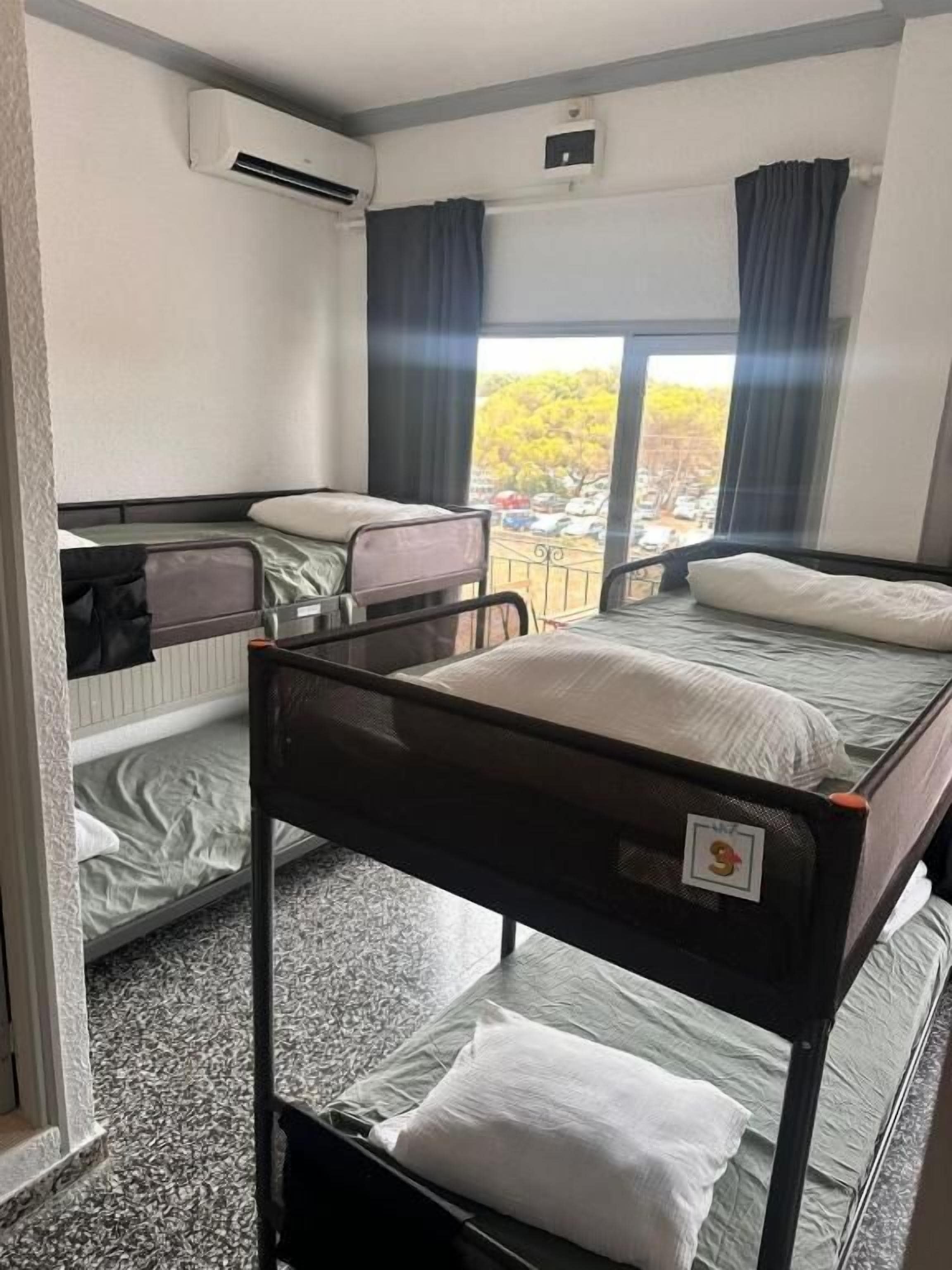 Habitación de hotel con literas, ventana con cortinas y un equipo de aire acondicionado.