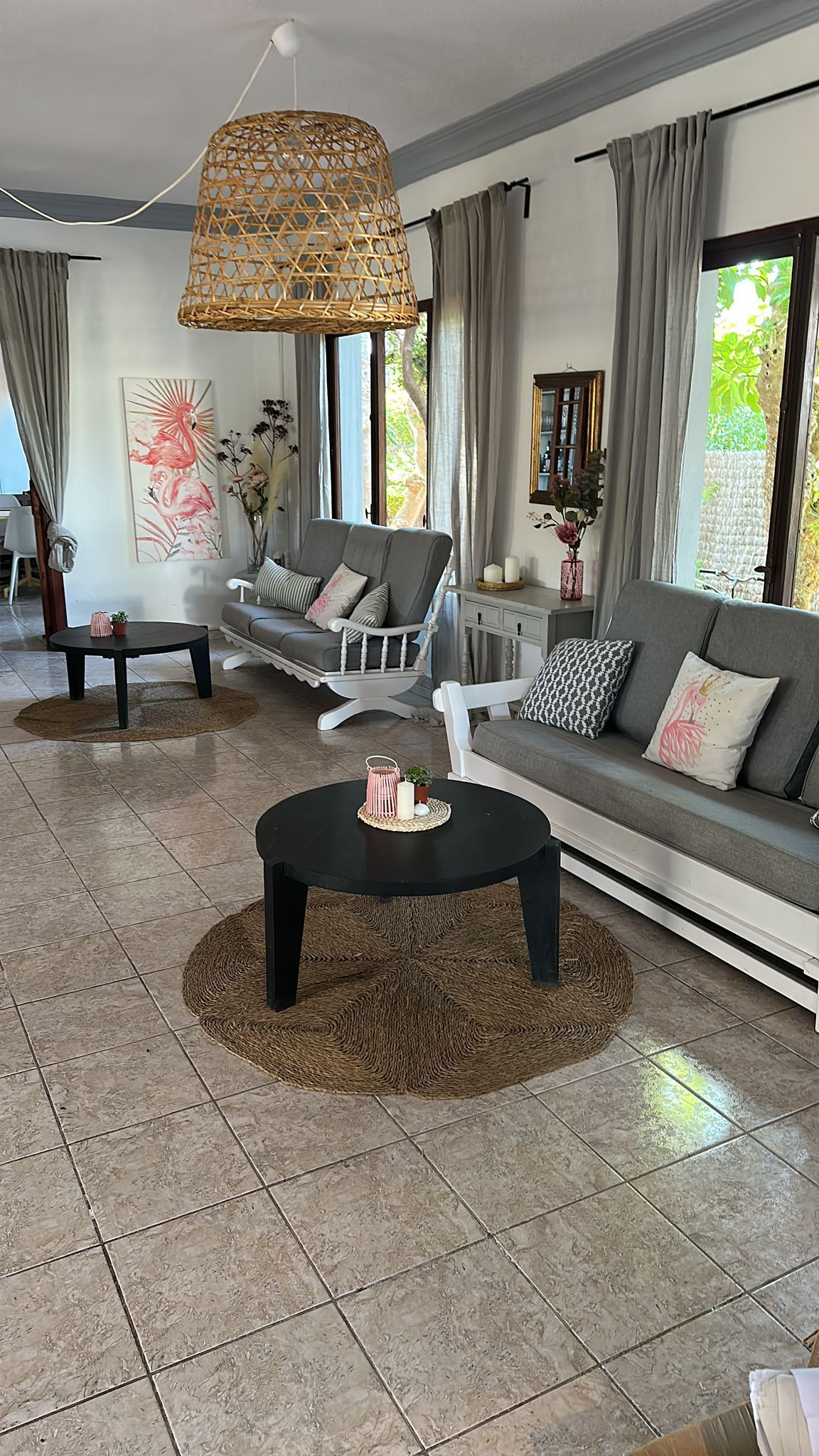 Un salon moderne avec un canapé gris, deux fauteuils, une table basse et une lampe suspendue en osier.