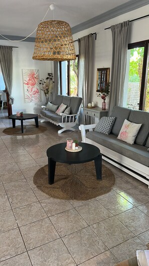 A modern living room with a grey sofa, two armchairs, a coffee table, and a hanging wicker lamp. - Flamingo by Nest (Santa Eulalia del Rio)
