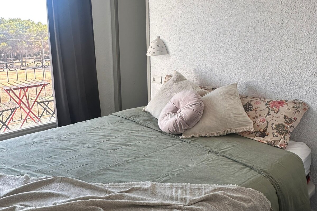 Habitación de hotel con cama, ventana con cortinas, unidad de aire acondicionado y vistas al exterior.