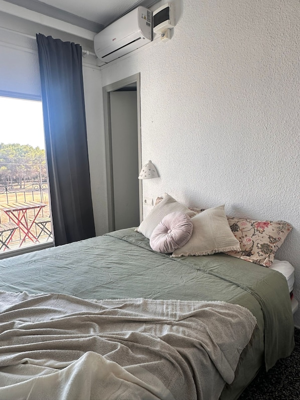 A hotel room with a bed, a window with curtains, an air conditioning unit, and a view of the outdoors.
